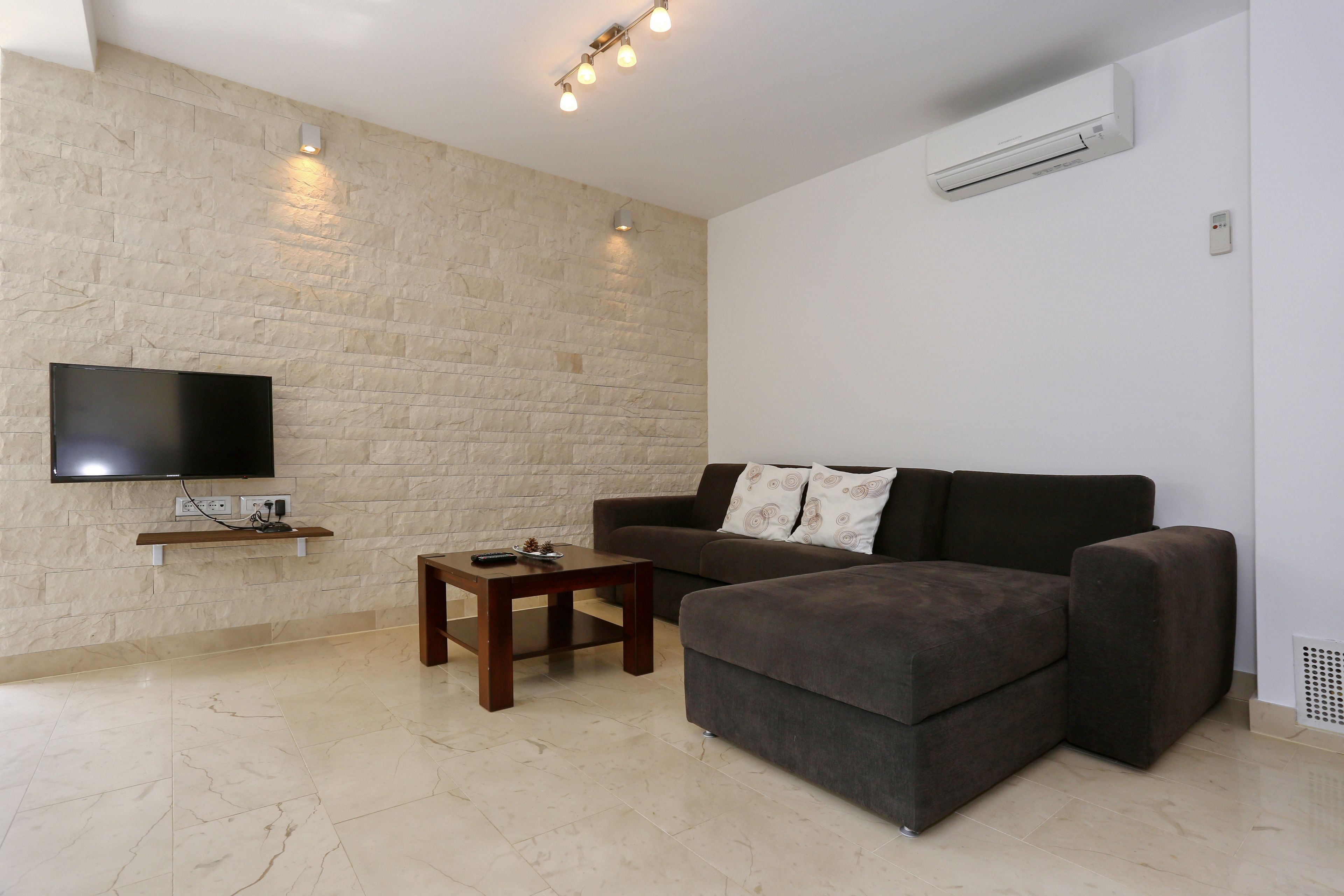 A modern living room with a stone wall, a flat-screen TV, a dark-colored sofa, and a small wooden coffee table.