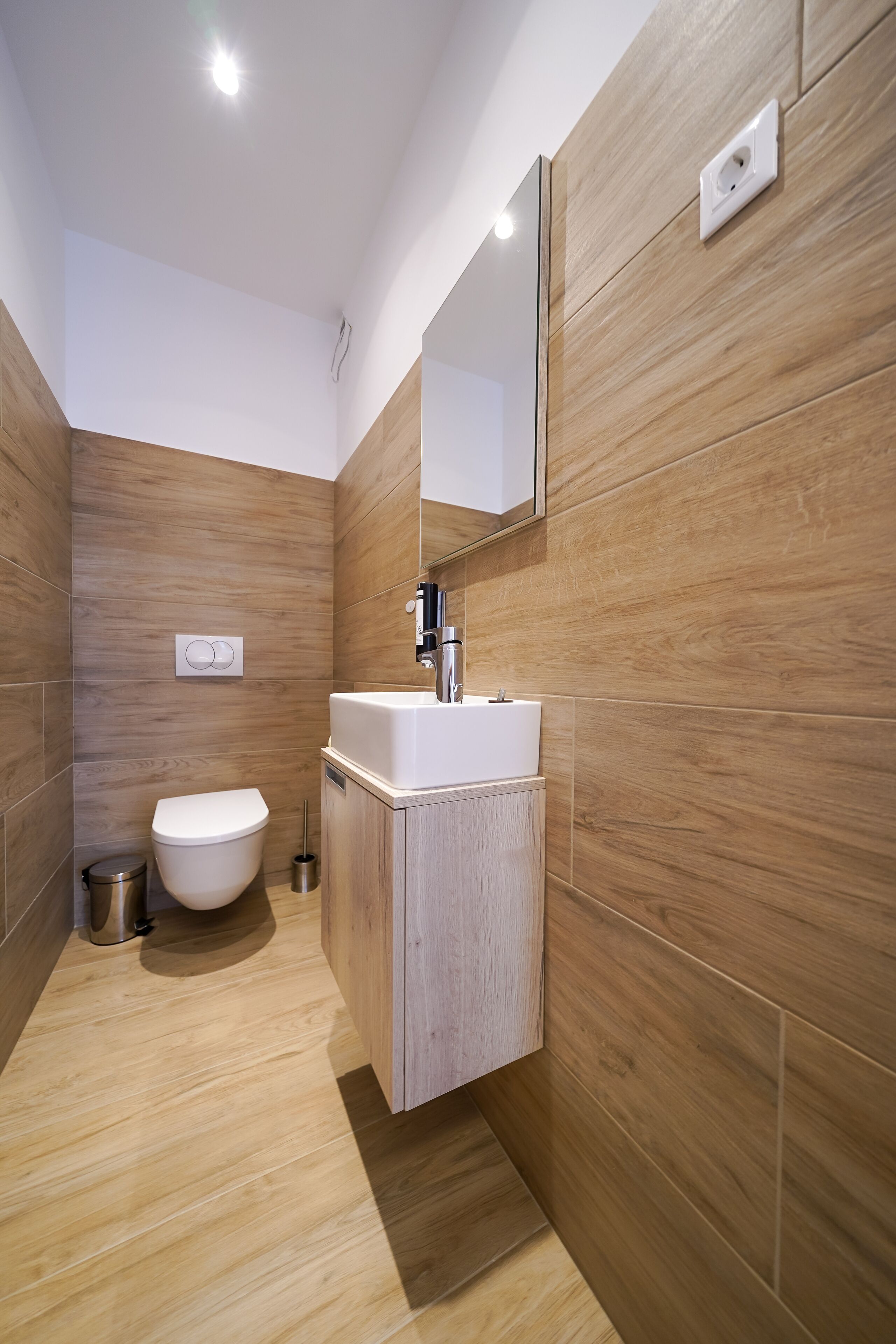 Ein modernes Badezimmer mit Holzwänden, einem weißen Waschbecken und einer Toilette.