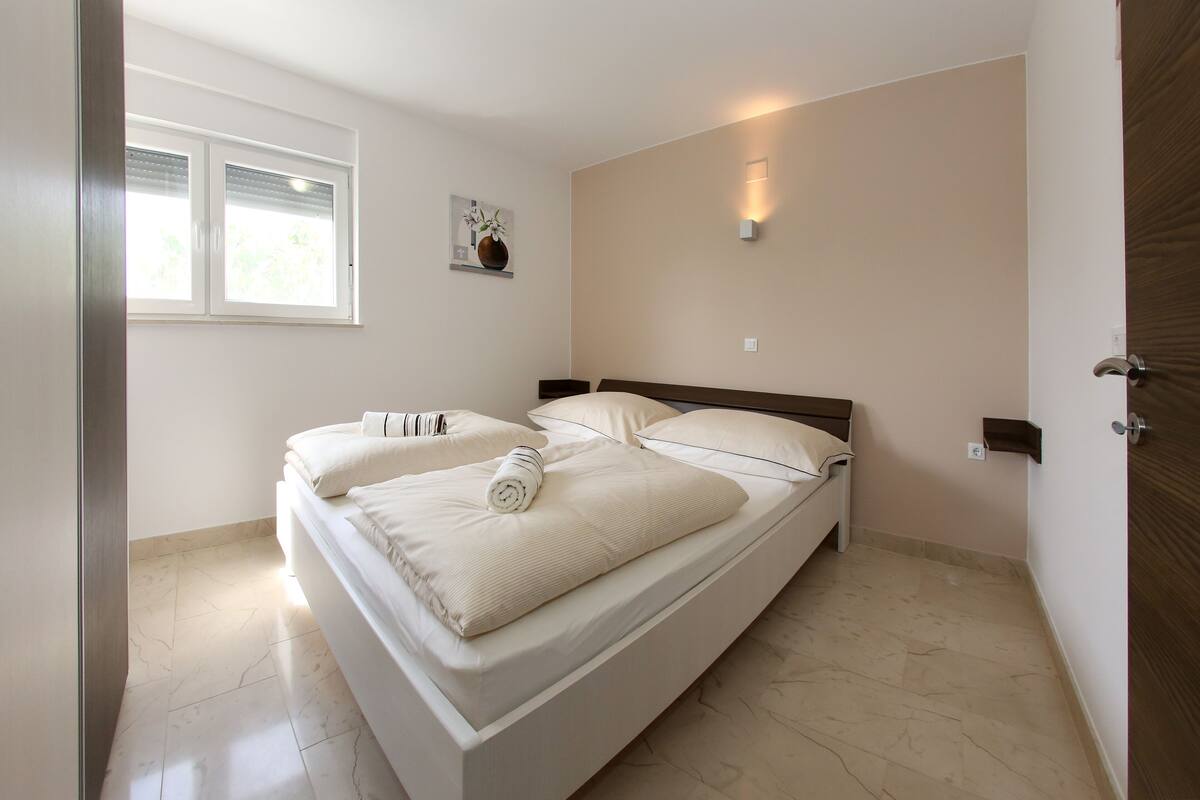 A bedroom with a bed, a window, and a wall-mounted light.