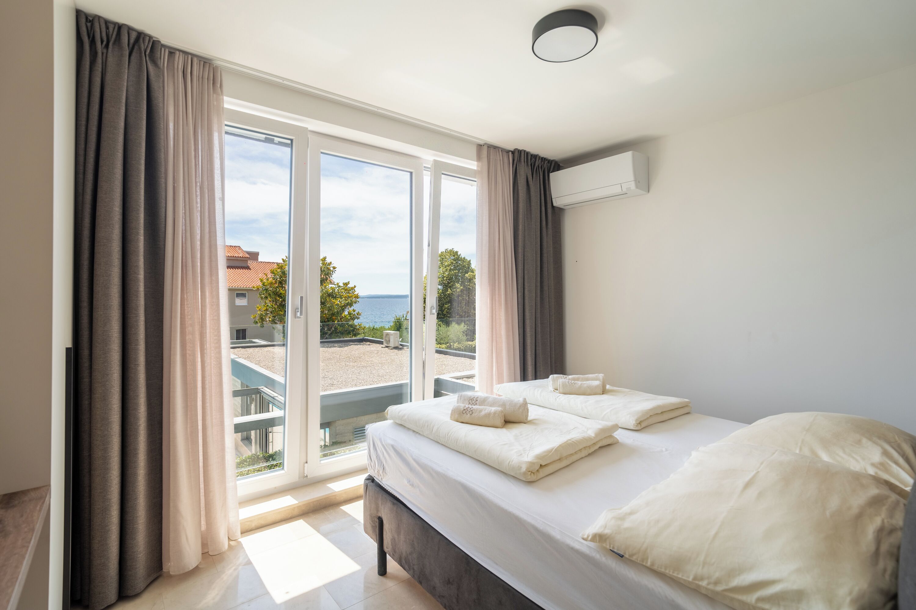 A bedroom with a bed, curtains, and a view of a beach and buildings.