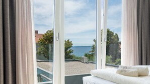 Une chambre à coucher avec un lit, une vue sur la mer et un balcon avec des rideaux.