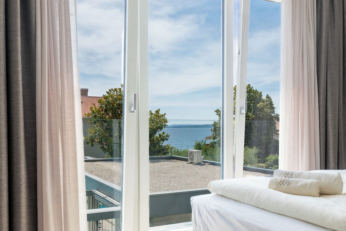 A bedroom with a bed, a view of the sea, and a balcony with curtains.