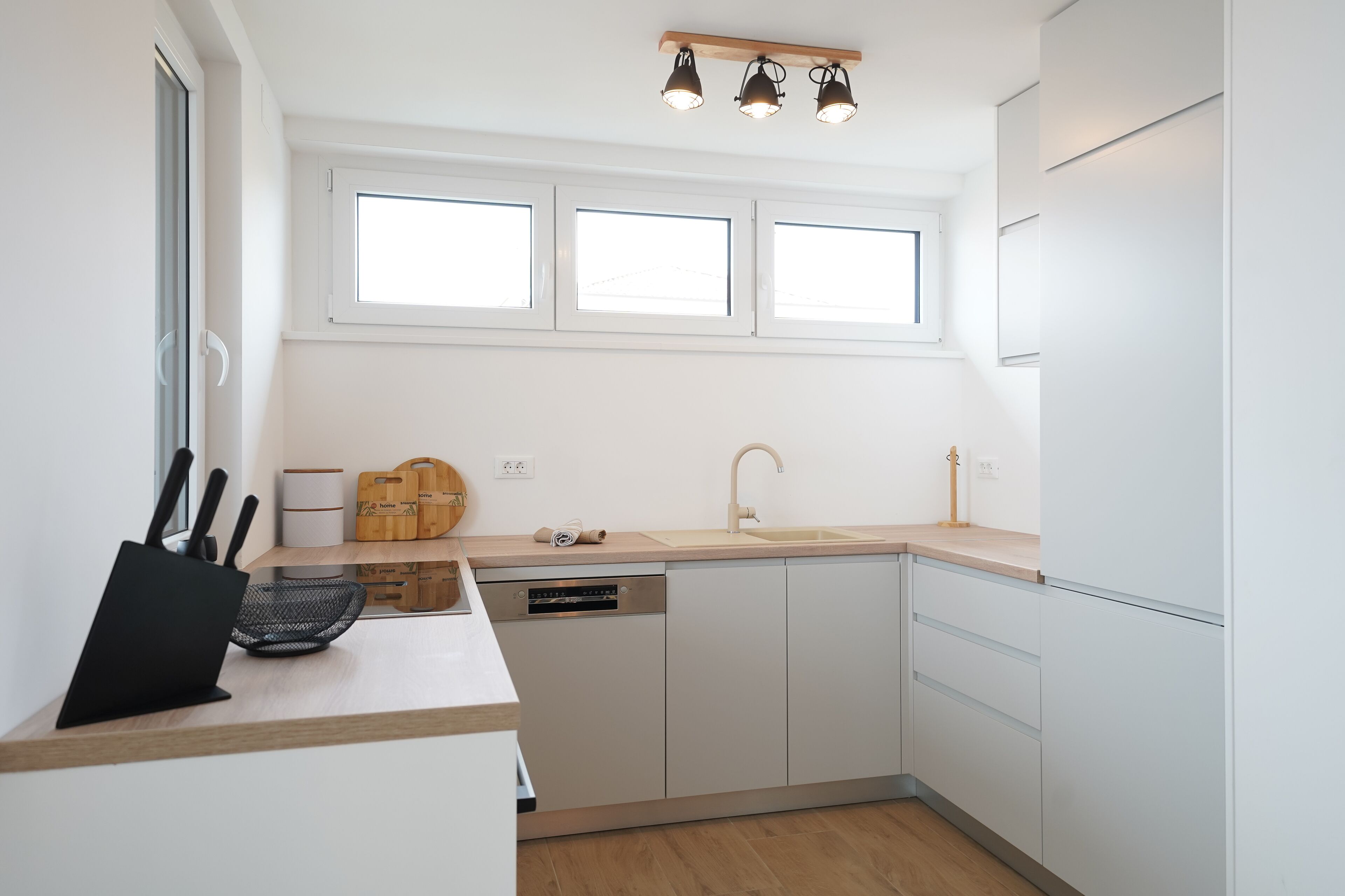 A modern kitchen with white cabinets, a dishwasher, and a window above the sink.