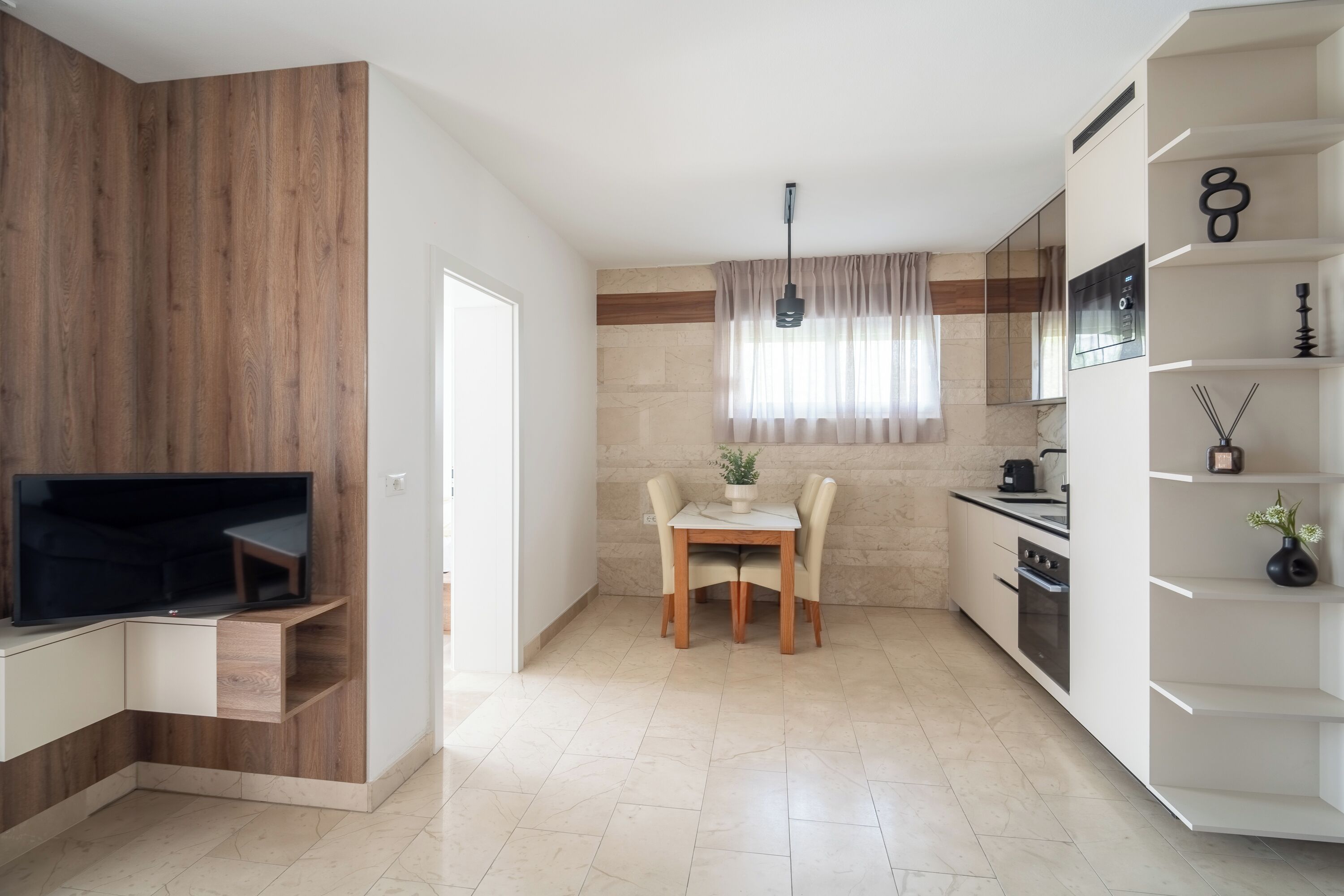 A modern kitchen with a built-in oven, a dining area with a table and chairs, and a TV mounted on a wooden cabinet.
