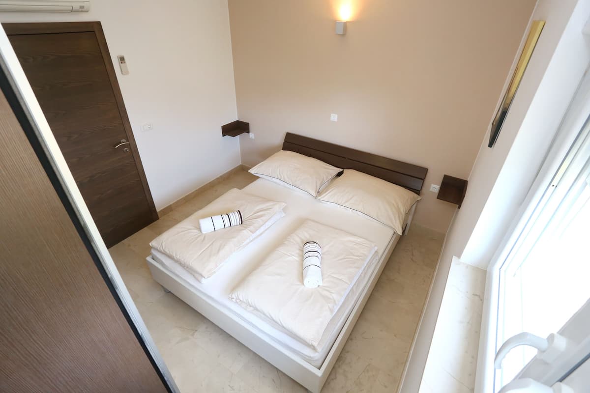 A neatly made bed with pillows and a blanket, a bedside table, a wall-mounted light, and a door.