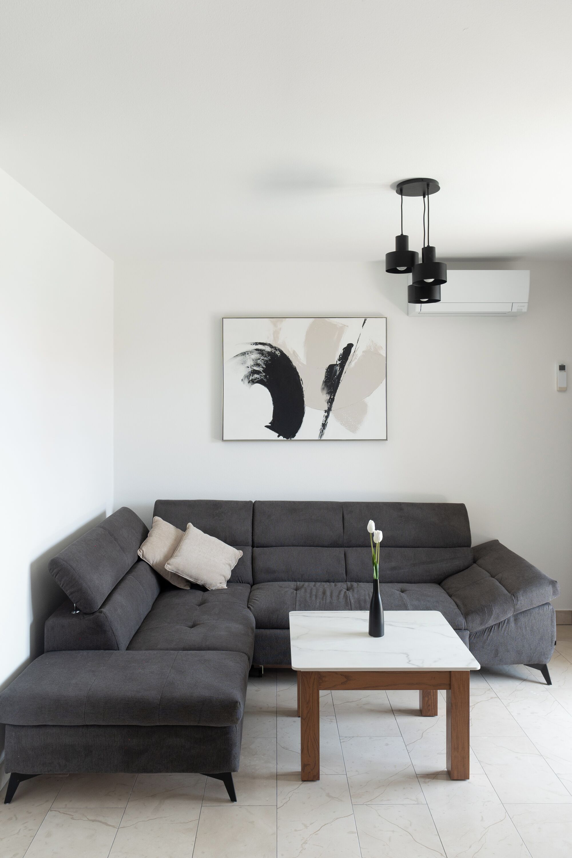 A modern living room with a grey sectional sofa, a white coffee table, and a black abstract painting on the wall.
