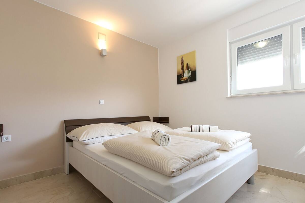A bedroom with a bed, a wall-mounted light, a window, and a painting.