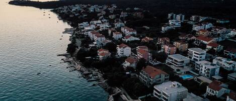 An aerial view of a coastal residential area with buildings along the shoreline, a clear sky, and a calm sea.