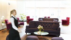 En modern entréhall med en mörkbrun soffa, röda stolar och ett runt soffbord med en vas med blommor.