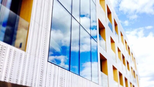 Un edificio moderno con fachada de vidrio, patrones geométricos en las ventanas y vista despejada al cielo.