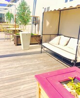 Una terraza de madera con un área de estar techada, una mesa con sillas y plantas en macetas.