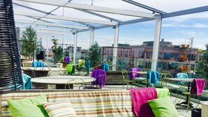 Ett utomhusområde med sittplatser, inklusive en bekväm bänk, en eldstad och en täckt uteplats med bord och stolar.