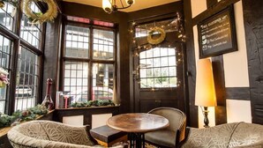 A cozy corner with a round table and two patterned chairs, a black door with a wreath, and a sign offering free Wi-Fi. - The Cardinals Hat (Worcester)