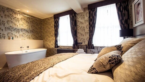 A bedroom with a large bed, a bathtub, and a window with curtains. - The Cardinals Hat (Worcester)