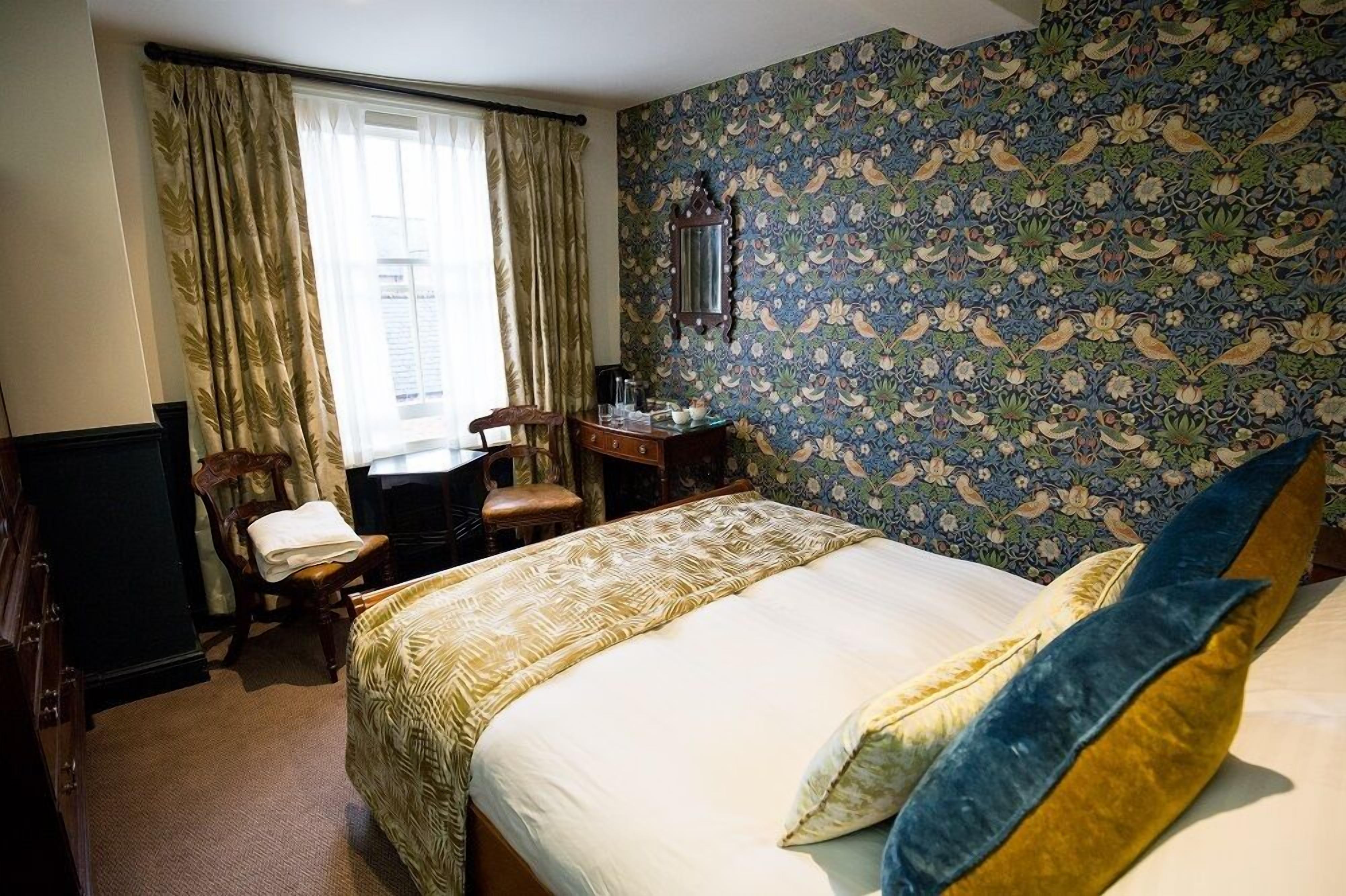 Une chambre d’hôtel avec un lit, un bureau, une chaise et une fenêtre avec des rideaux.