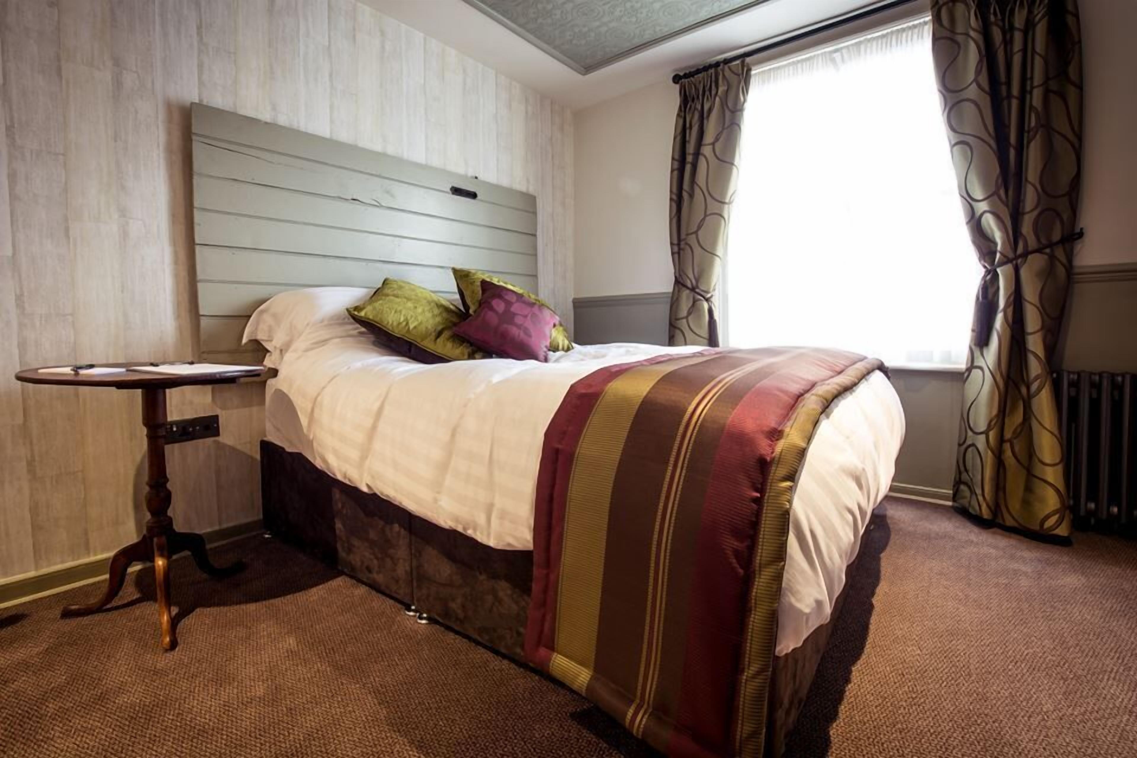 Ein Hotelzimmer mit Bett, Nachttisch, Fenster mit Vorhängen und Heizkörper.