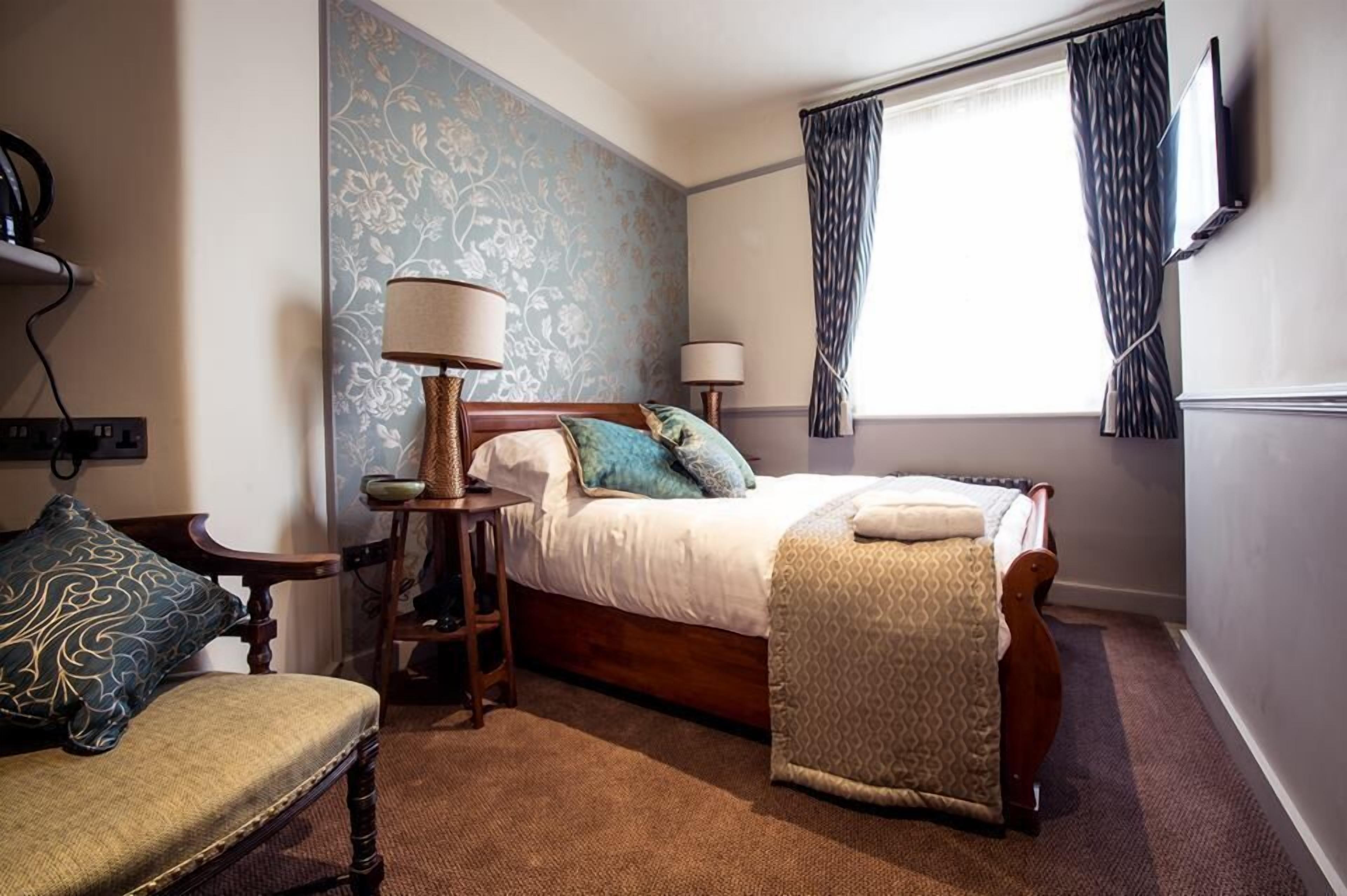 Een hotelkamer met een bed, twee bedlampen, een stoel, een klein tafeltje en een kamerbreed tapijt met patroon.