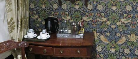 Una stanza con carta da parati a motivi, una scrivania in legno con uno specchio, una sedia, un cestino e una macchina da caffè.