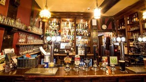 A bar with multiple beer taps, shelves of bottles, and a clock on the wall. - The Cardinals Hat (Worcester)