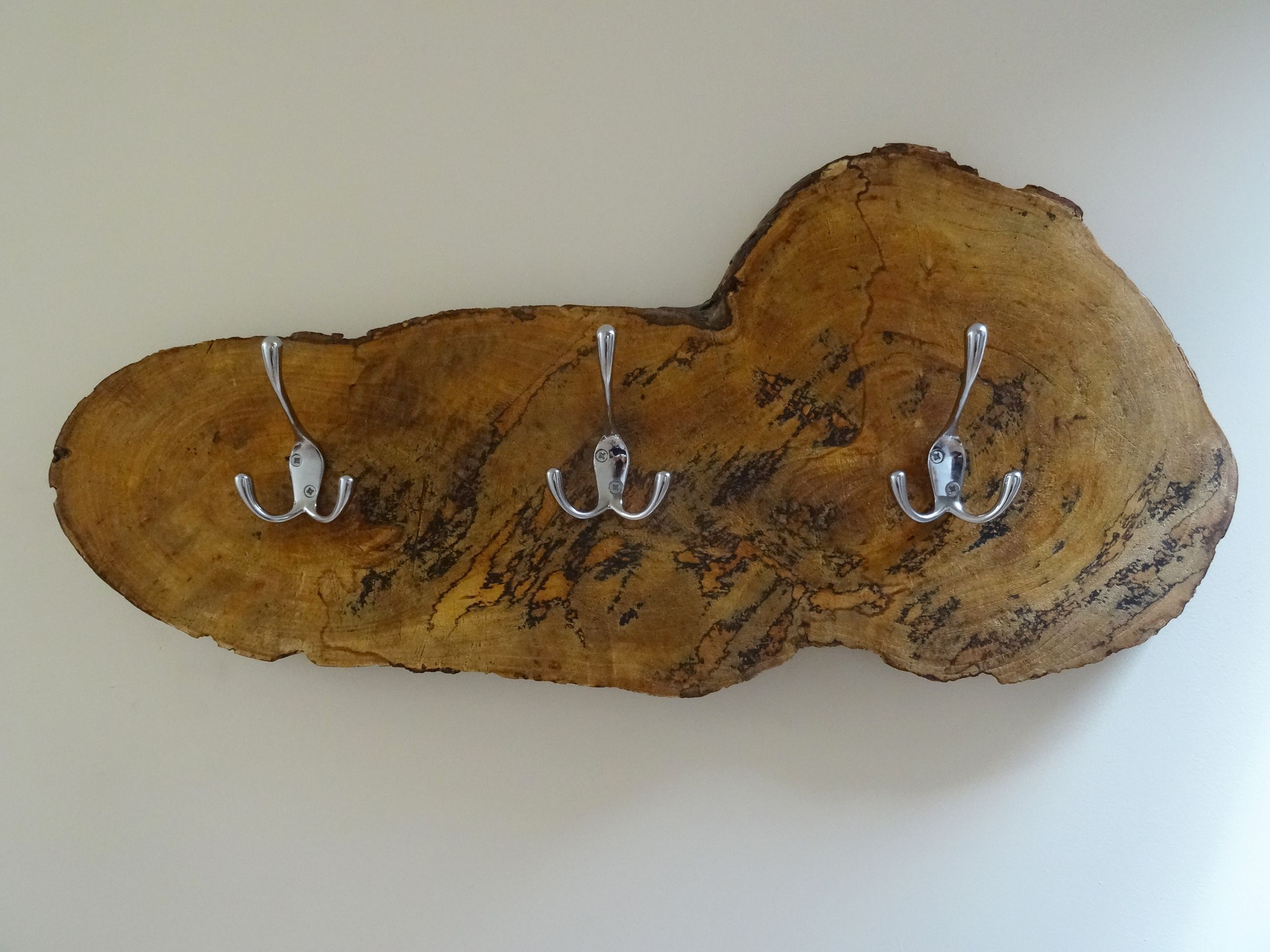 Un adorno de madera fijado a la pared con tres ganchos metálicos.