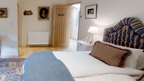 A bedroom with a bed, a nightstand, a lamp, a patterned headboard, a door, and a radiator. - Hollamoor Farm B&B (Barnstaple)