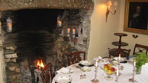 A dining room with a stone fireplace, a table set for a meal, and a portrait on the wall. - Hollamoor Farm B&B (Barnstaple)