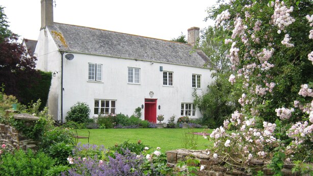 A white house with a red door, surrounded by a garden with various flowers and a stone wall. - Hollamoor Farm B&B (Barnstaple)