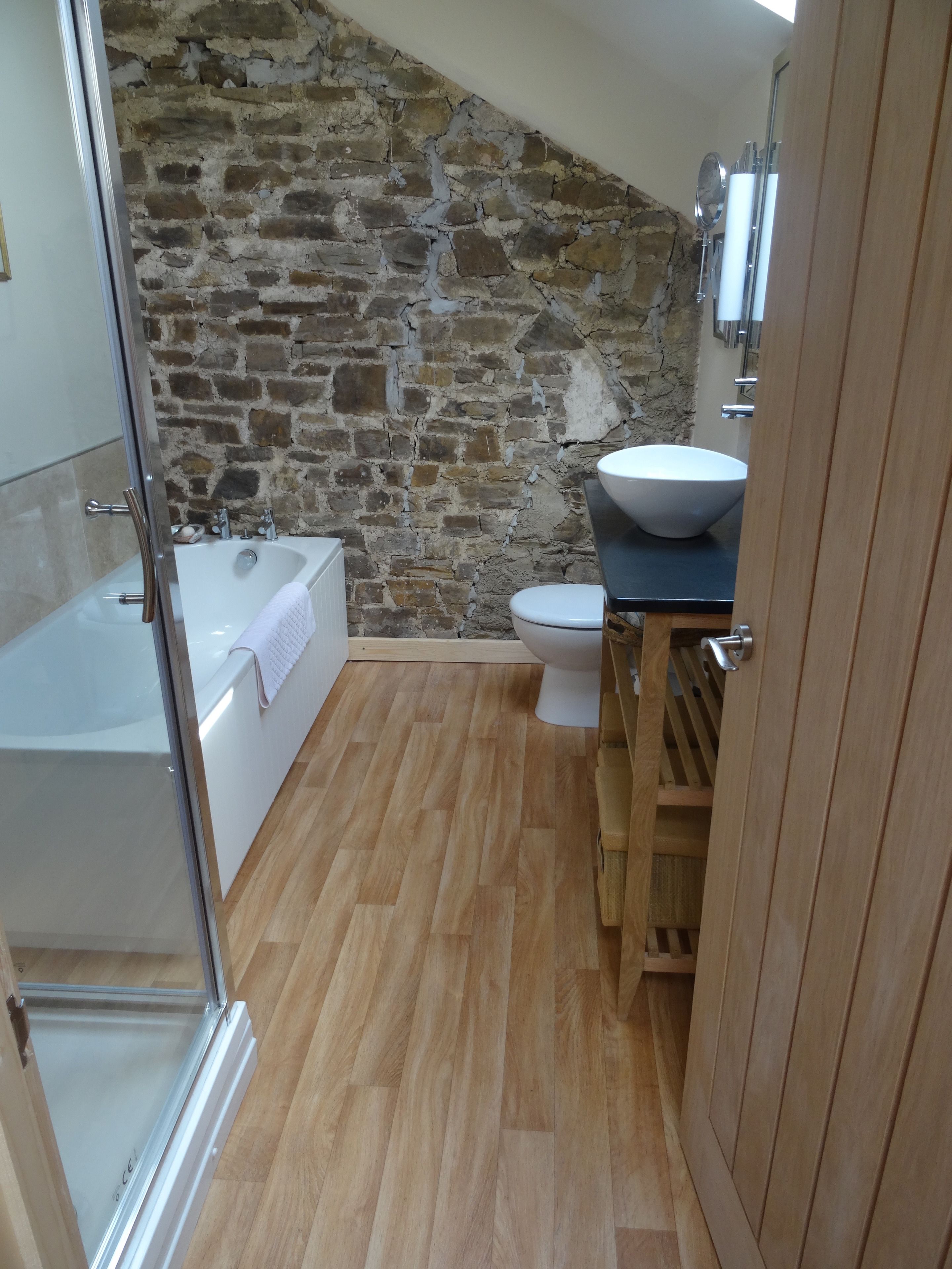 A bathroom with a stone wall, a bathtub, a toilet, and a wooden cabinet.