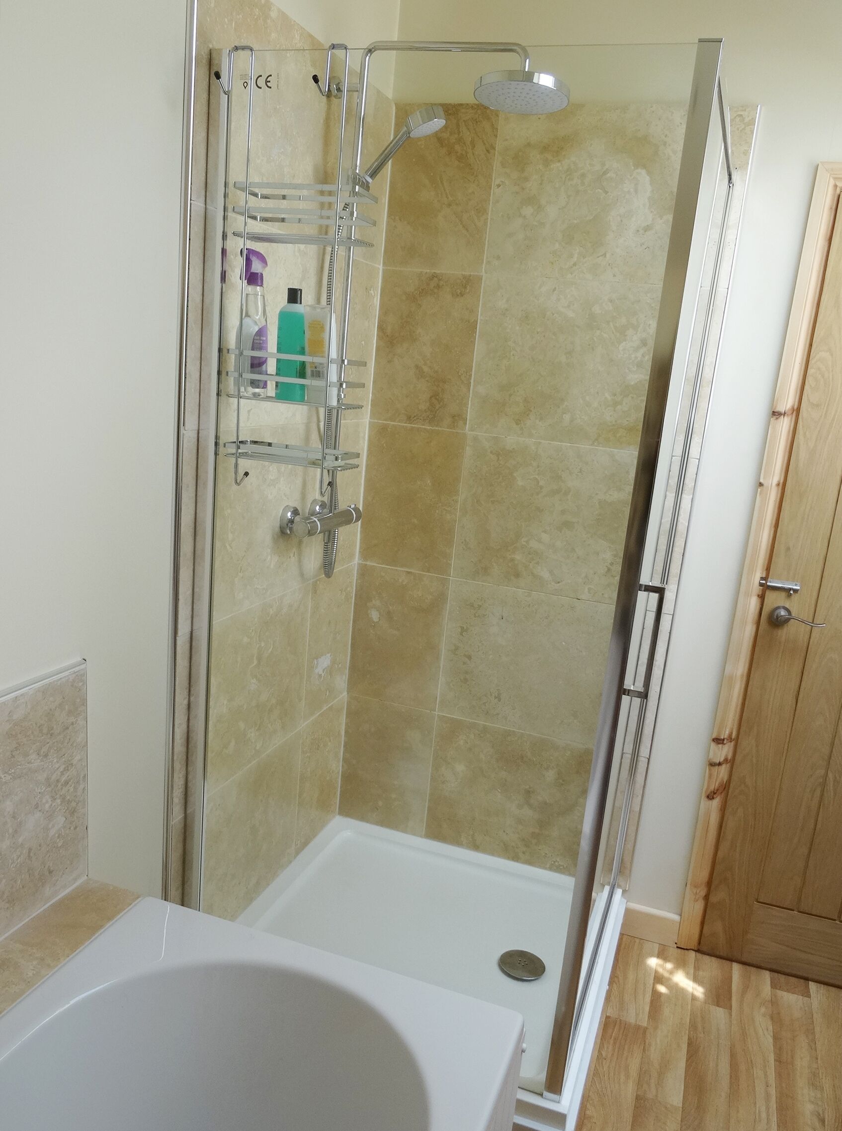 A shower with a glass door, a white bathtub, and a wooden door.