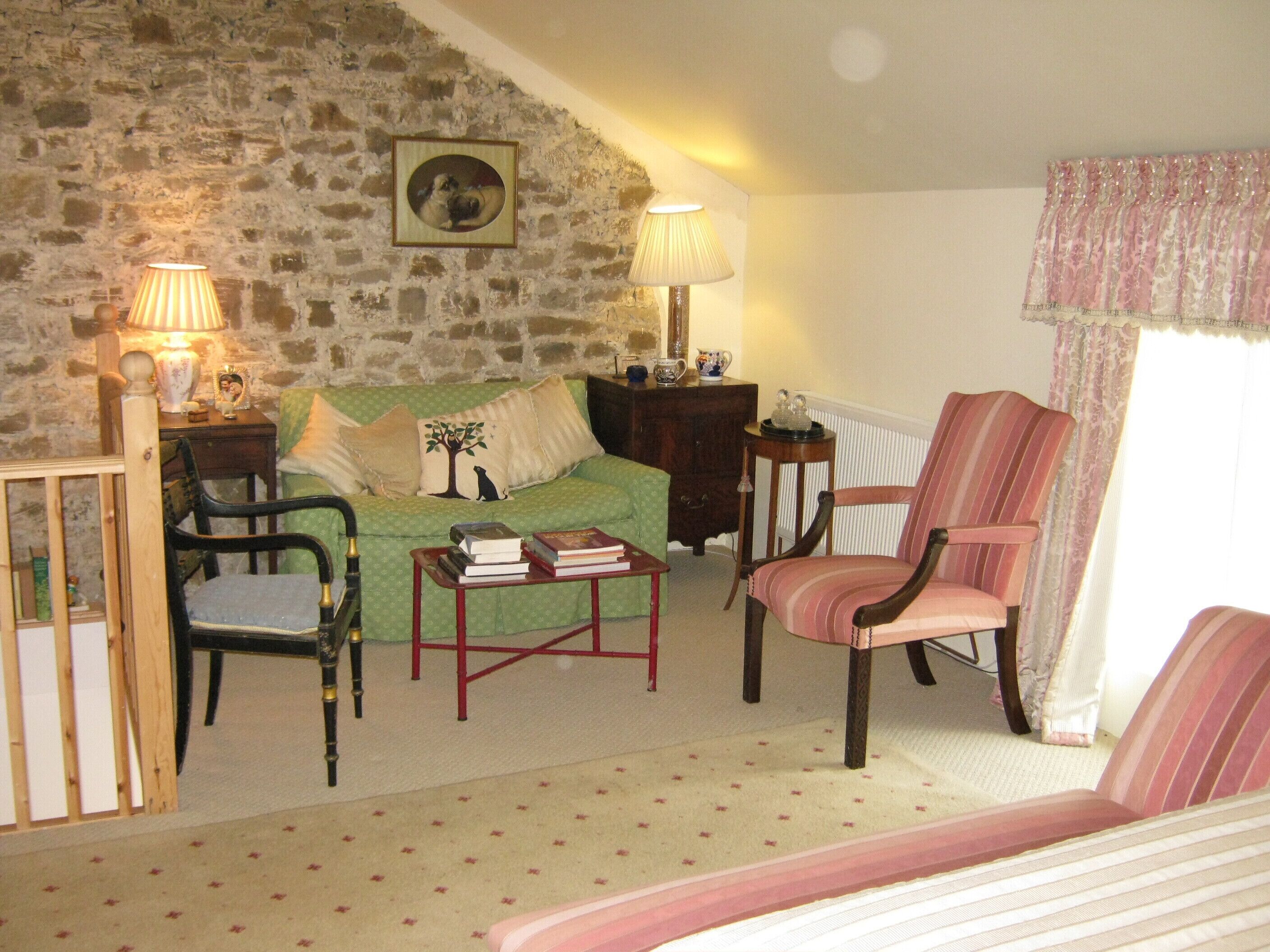 Una sala de estar acogedora con una pared de piedra, un sofá verde, un sillón a rayas, una mesa de centro de madera y dos lámparas.