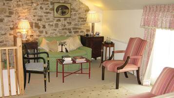 Una sala de estar acogedora con una pared de piedra, un sofá verde, un sillón a rayas, una mesa de centro de madera y dos lámparas.