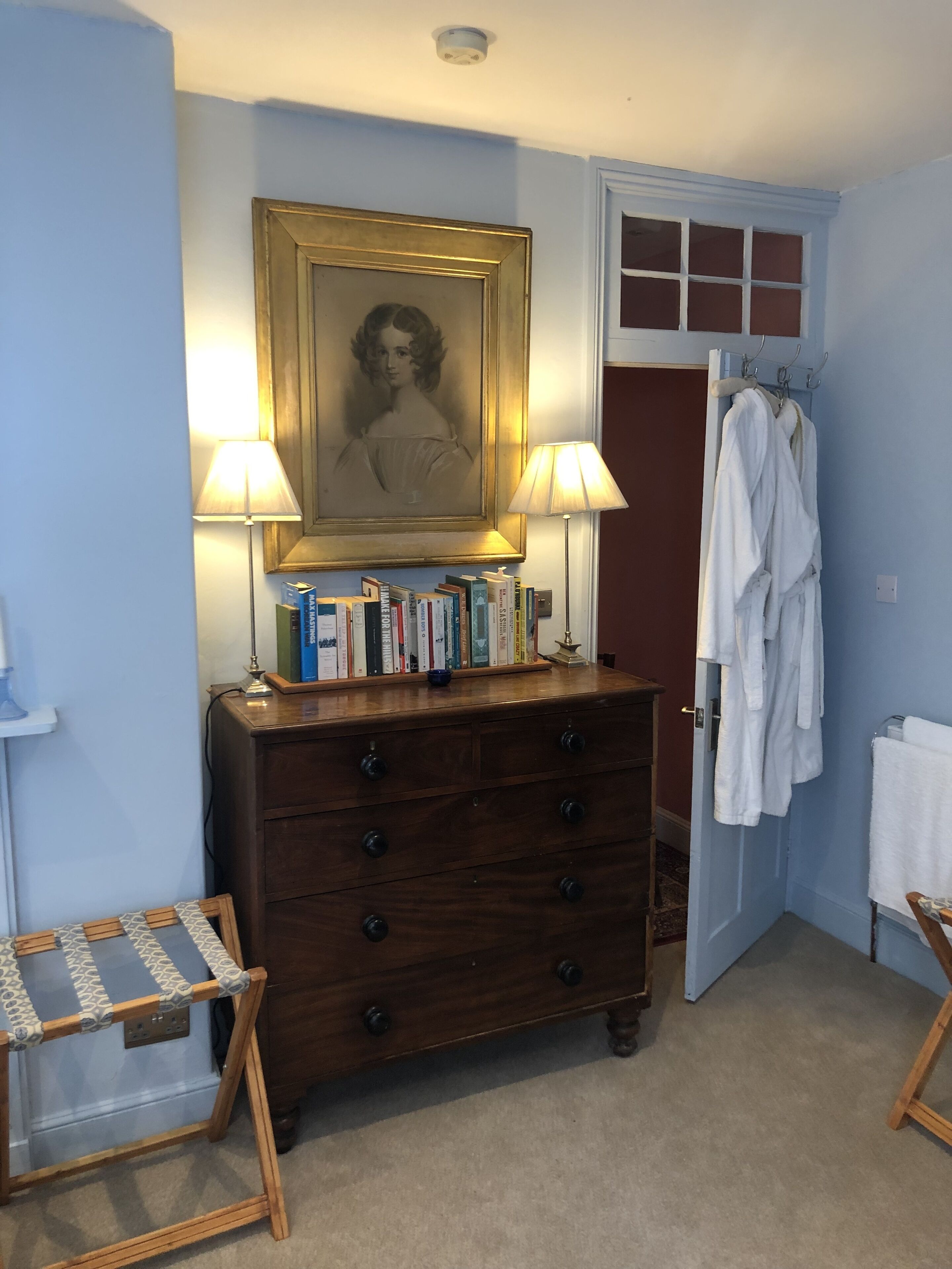 A room with a wooden dresser, books, a framed portrait, and a robe rack.