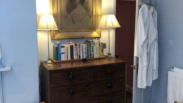 A room with a wooden dresser, books, a framed portrait, and a robe rack.