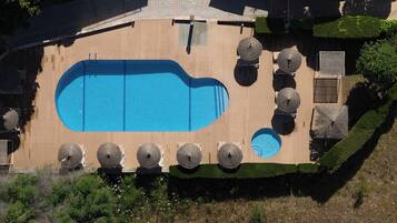 Vista aérea de una piscina con muelle de madera, rodeada de sillas de descanso y sombrillas.
