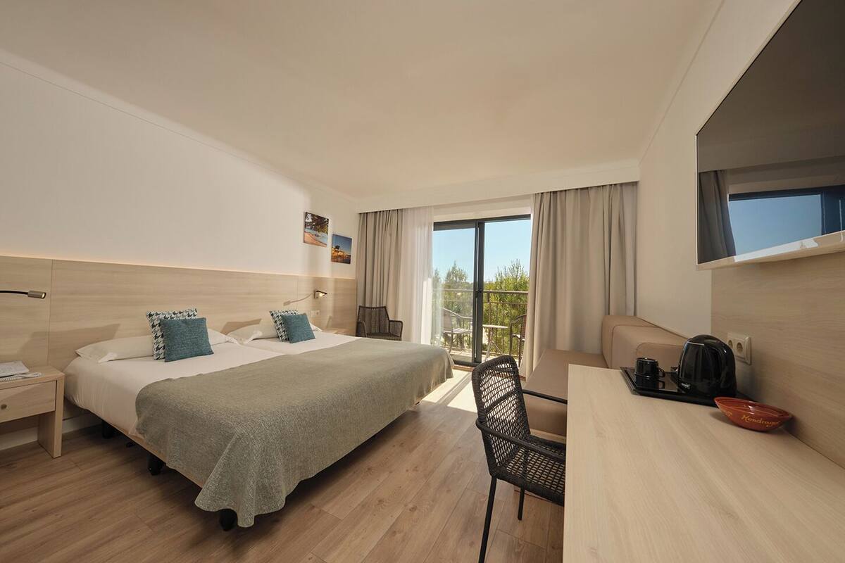 A hotel room with a bed, a desk, a chair, a nightstand, and a balcony with a view.