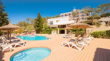 Una piscina al aire libre, sombrillas, sillones reclinables de piscina