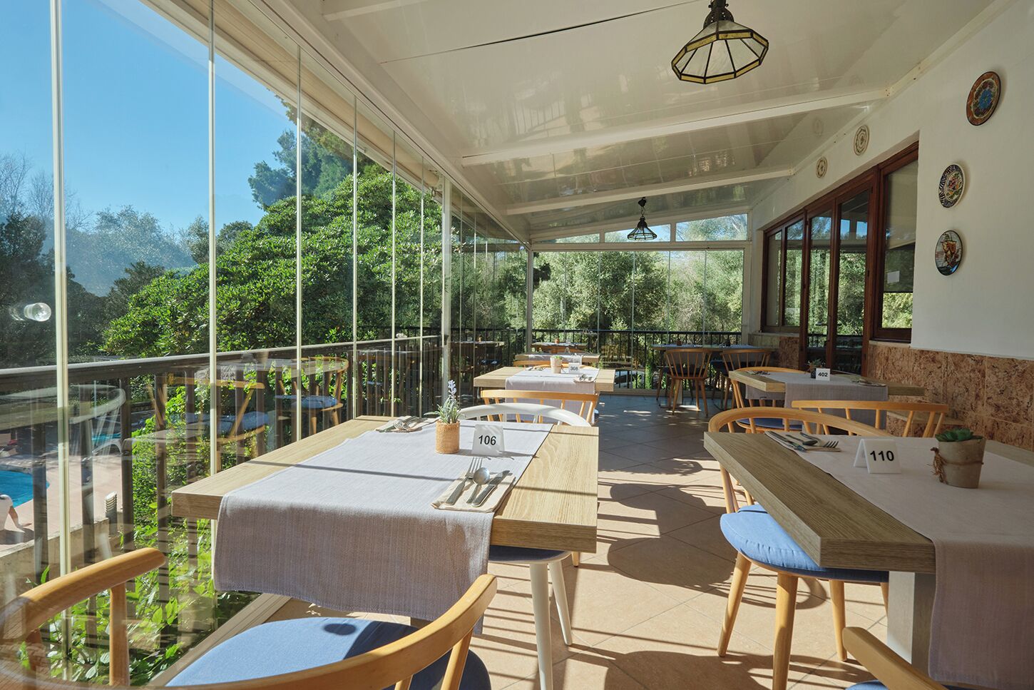 A restaurant with outdoor seating overlooking a pool, featuring a glass enclosure and wooden furniture.