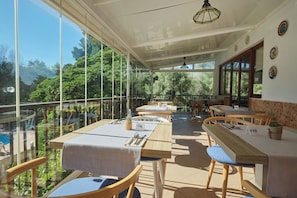 Restaurante con terraza al aire libre y vistas a una piscina, con cerramiento de cristal y mobiliario de madera.