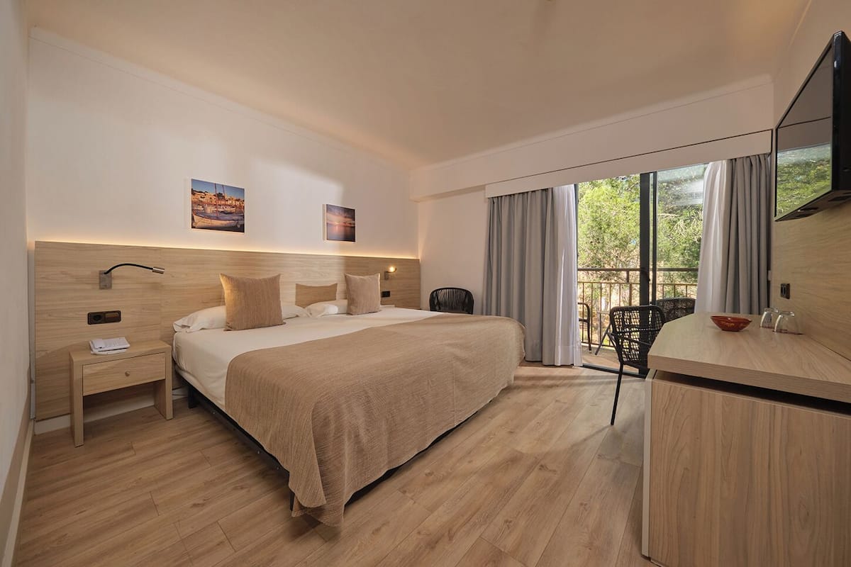 A modern hotel room with a large bed, a desk, a chair, and a TV.