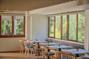 A dining area with tables and chairs, large windows with a view of trees, and a sloped ceiling. - Hotel Playa Mondrago (Santanyi)