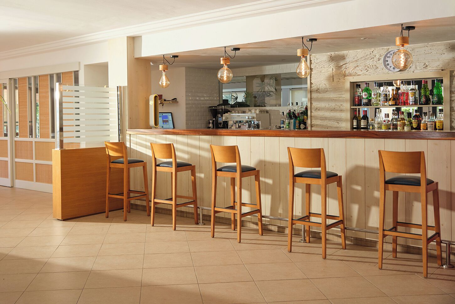 Un espace bar avec des tabourets en bois, un comptoir et des luminaires suspendus.