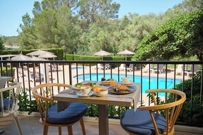 A dining table with plates of food, a cup, and a glass of orange juice on a balcony overlooking a swimming pool and lounge chairs. - Hotel Playa Mondrago (Santanyi)