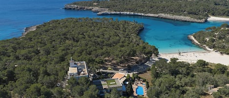 Vue aérienne d’une propriété située sur la côte, avec une piscine, une plage et une forêt dense.