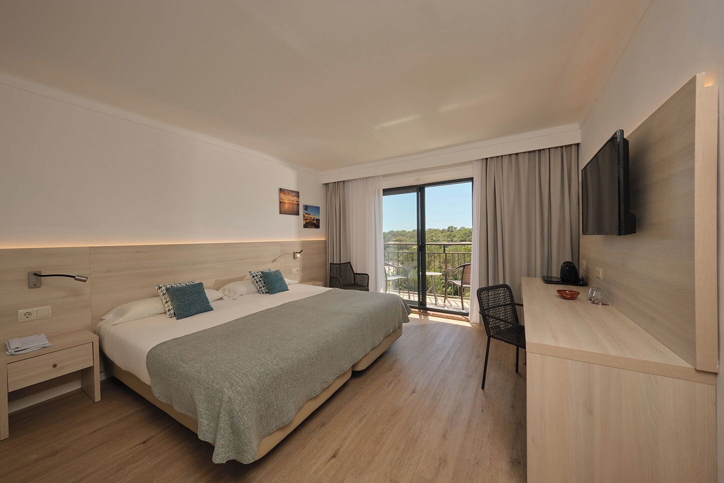 Una habitación de hotel moderna con una cama grande, un escritorio, una silla, un televisor y un balcón con vistas.
