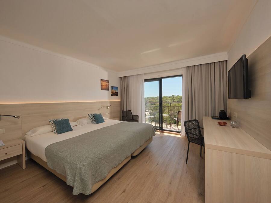 Una habitación de hotel moderna con una cama grande, un escritorio, una silla, un televisor y un balcón con vistas.