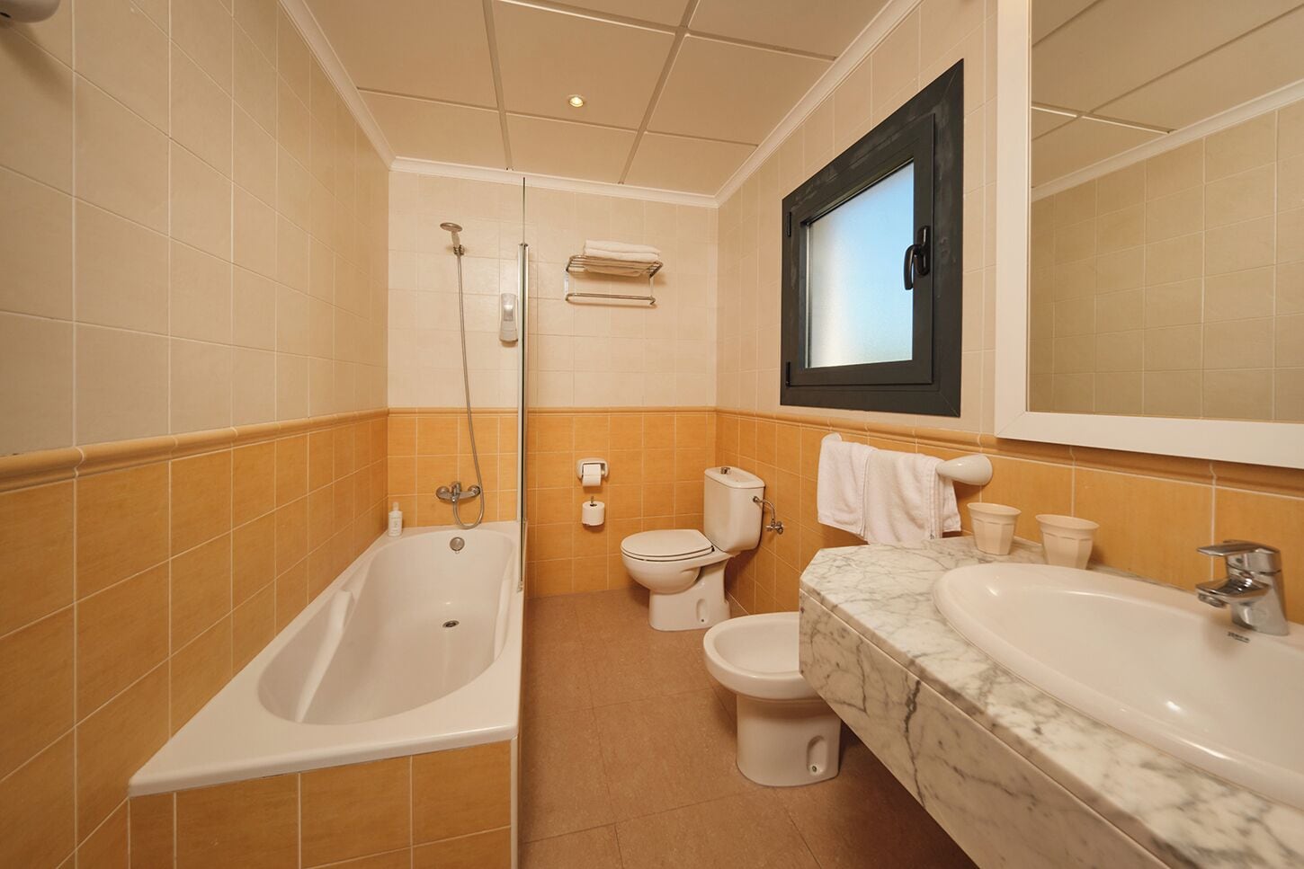 A bathroom with a bathtub, toilet, bidet, and a sink with a marble countertop.