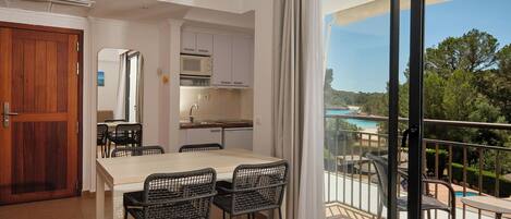 Una habitación con una mesa de comedor, sillas, zona de cocina y balcón con vistas a la playa y la piscina.