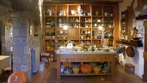 A rustic kitchen with wooden shelves filled with dishes and utensils, a central island with a sink, and stone walls.