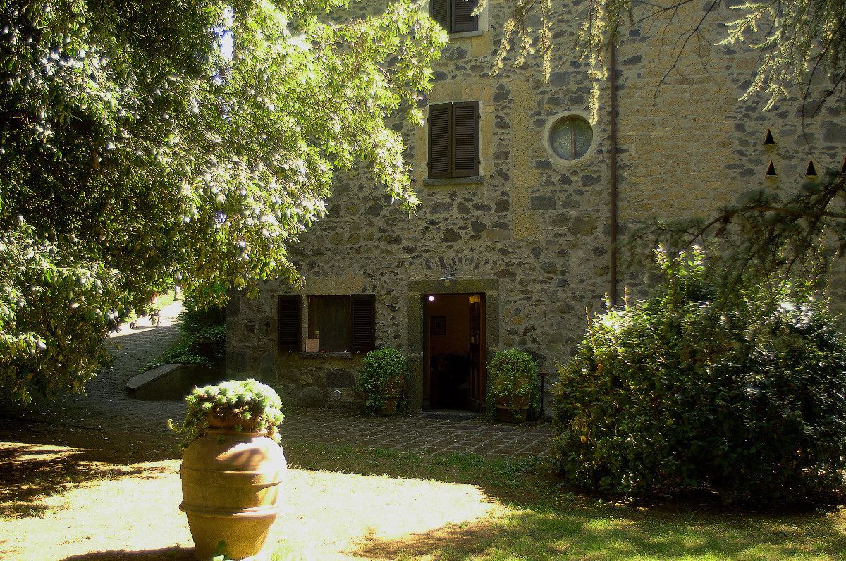 A stone building with a courtyard, a large planter, and a small door.