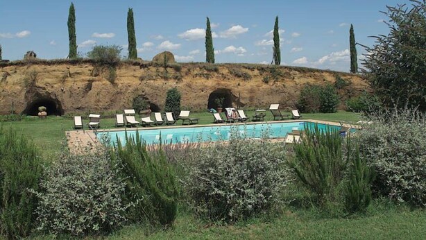 A pool area with lounge chairs, a clear sky, and a rocky hillside with trees.